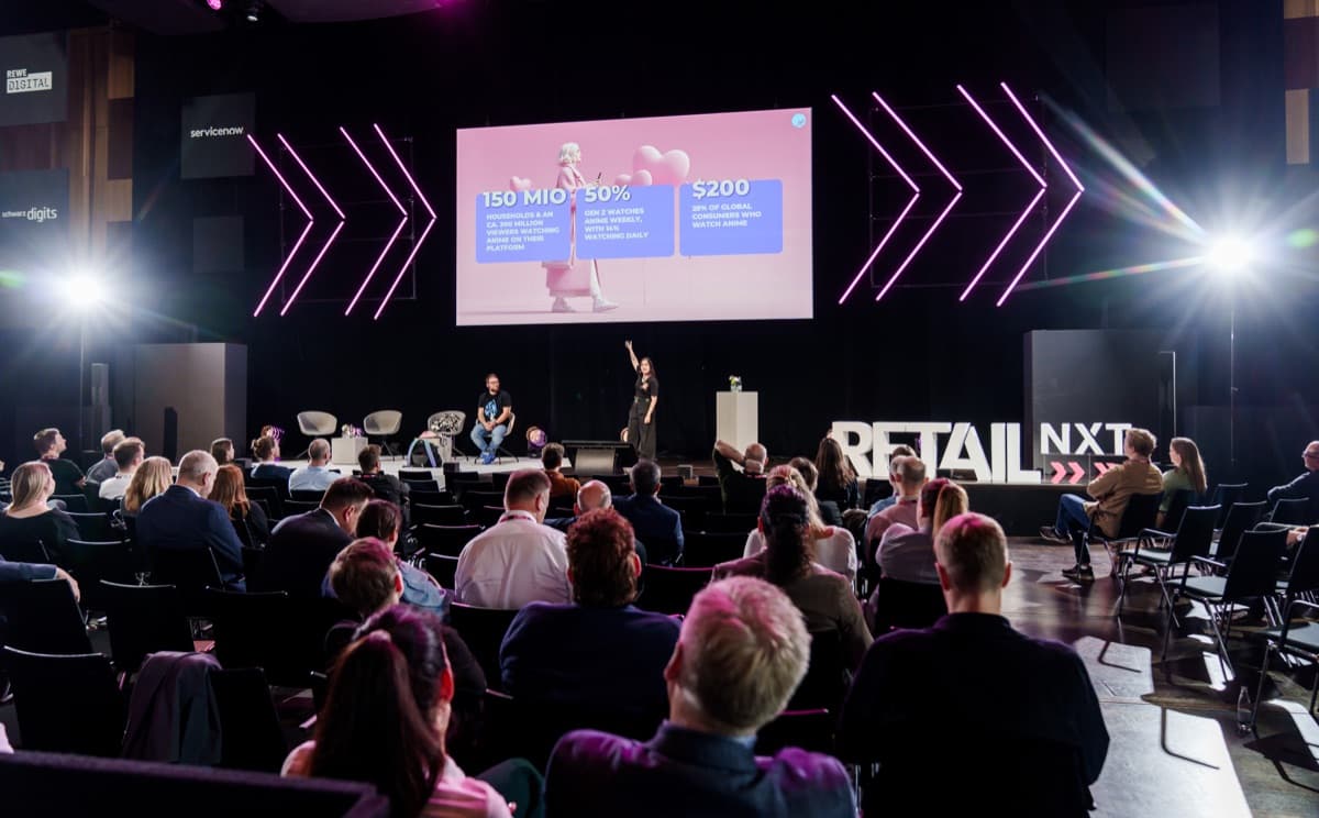 Jasmin on stage at Retail NXT, anime market figures on the screen behind her